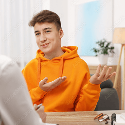 A smiling teenaged boy in an orange hoodie gestures with both his hands during a therapy session
