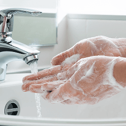 A close up of hands covered in soap under a water faucet